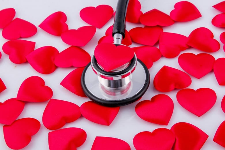 A stethoscope presses on a red heart-shaped object amid scattered red heart shapes on a white background.